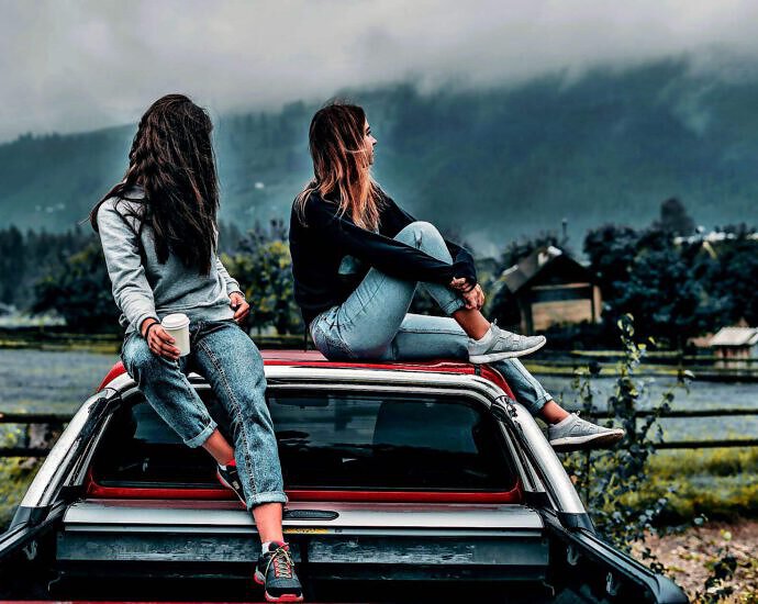 Zwei junge Frauen sitzen auf dem Dach eines Autos.