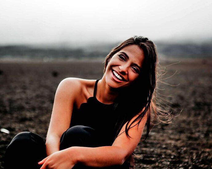 Eine schöne junge Frau steht in einer Landschaft und lacht fröhlich.