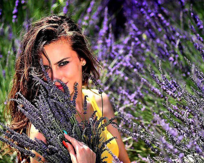 Eine junge Frau inmitten eines Lavendelfeldes und sie lacht vor Freude.