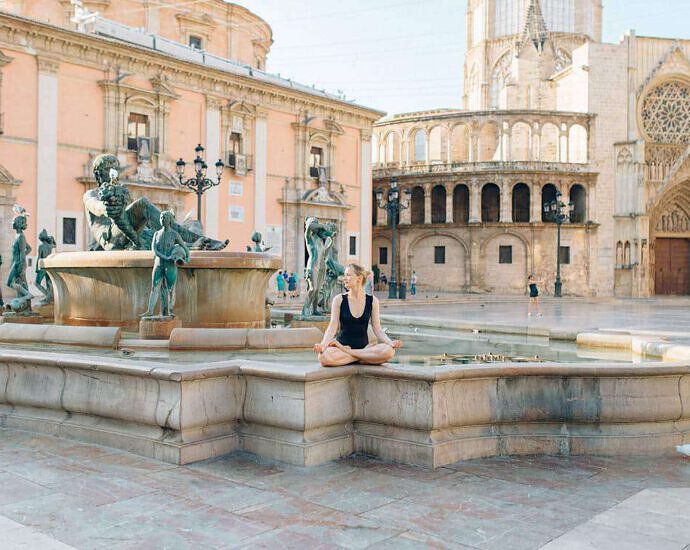 Eine junge Frau sitzt an einem Brunnen und meditiert.