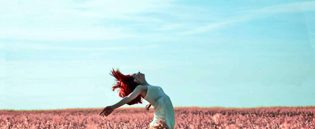 Eine Frau streckt vor Freude die Arme in die Luft. Sie steht in einem Blumenfeld.