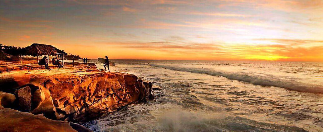 Bei Sonnenuntergang ist eine Person auf einem Felsen zu sehen. Vor ihr erstreckt sich das Meer.