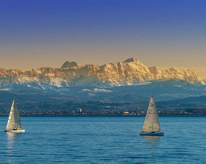 Ein Bild des Bodensees mit zwei Segelschiffen, im Hintergrund die Schweizer Berge.