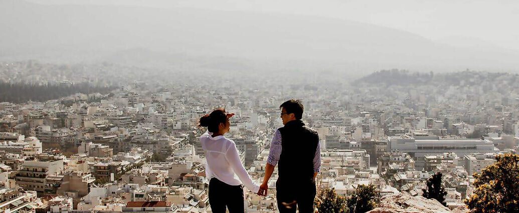 Ein Paar steht an einem Berghang und blickt auf eine Stadt unten im Tal.