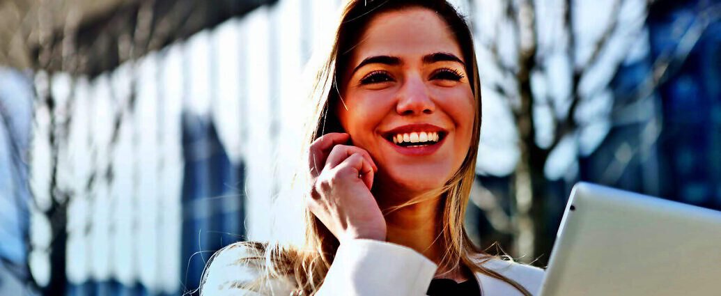 Eine junge Frau, die lacht und gleichzeitig mit dem Smartphone telefoniert.