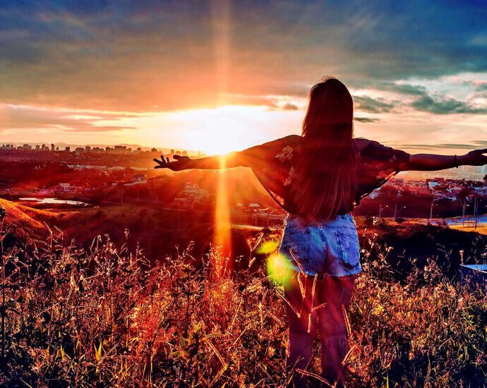 Eine junge Frau steht zum Sonnenuntergang und streckt die Arme aus.