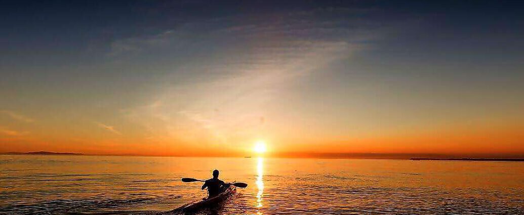 Ein Mann fährt mit dem Kanu auf dem Meer in Richtung Sonnenuntergang.