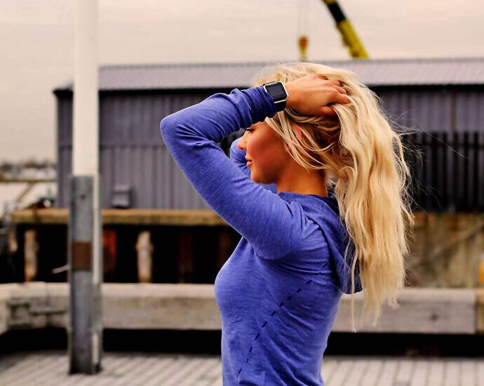 Eine junge Frau mit blonden Haaren hält die Arme über dem Kopf und wirkt entspannt.