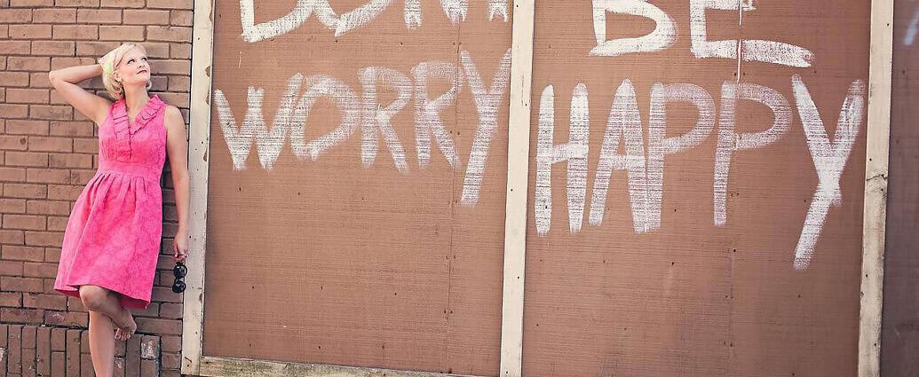Zu sehen ist ein Bild von einer jungen Frau, die in einem rosa Kleid an einer Mauer steht.