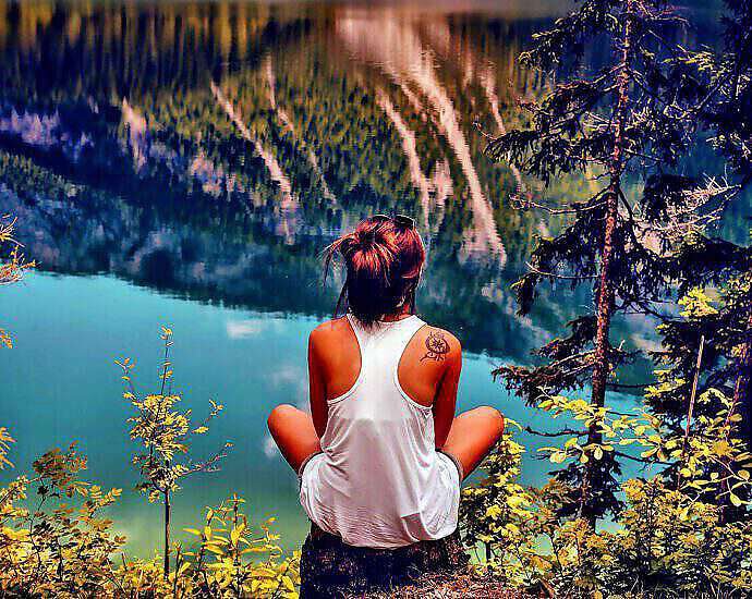 Eine junge Frau sitzt im Schneidersitz auf einem Felsvorsprung und schaut auf den Fluss unter ihr.