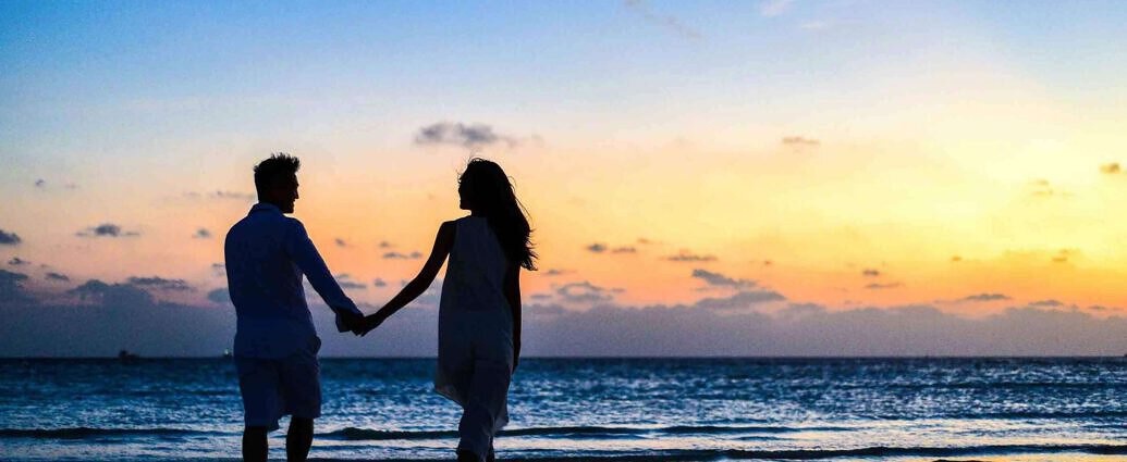 Ein verliebtes Liebespaar geht bei Sonnenuntergang Hand in Hand am Strand spazieren.