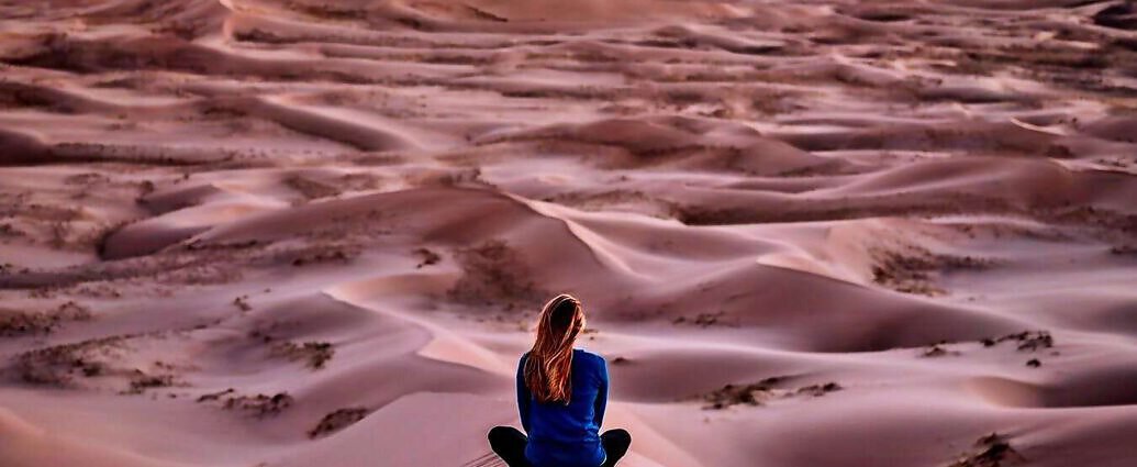 Eine junge Frau sitzt im Schneidersitz in der Wüste.
