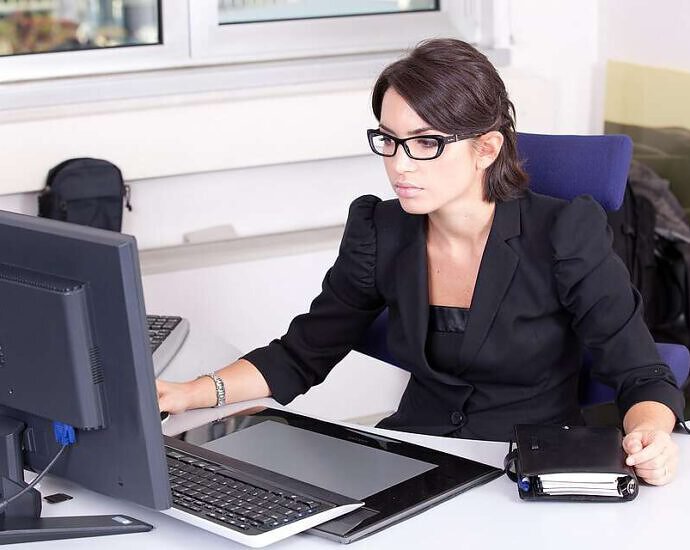 Eine junge Frau sitzt in ihrem Arbeitszimmer und schaut konzentriert auf den Monitor ihres Computers.