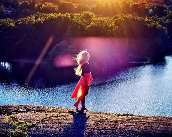 Eine junge Frau geht an einem See spazieren und schaut verträumt drein.