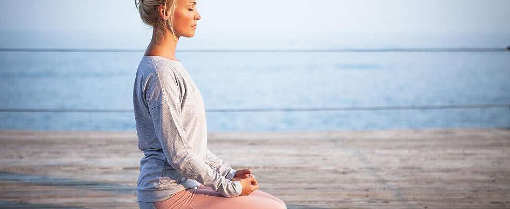 Eine junge Frau kniet auf dem Boden und meditiert.