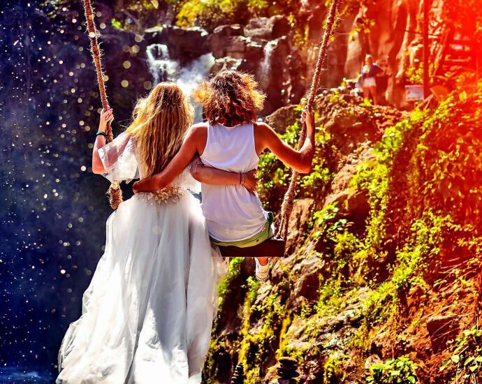 Zwei junge Frauen in weißen Kleidern schaukeln über eine Schlucht, mit einer Schaukel.