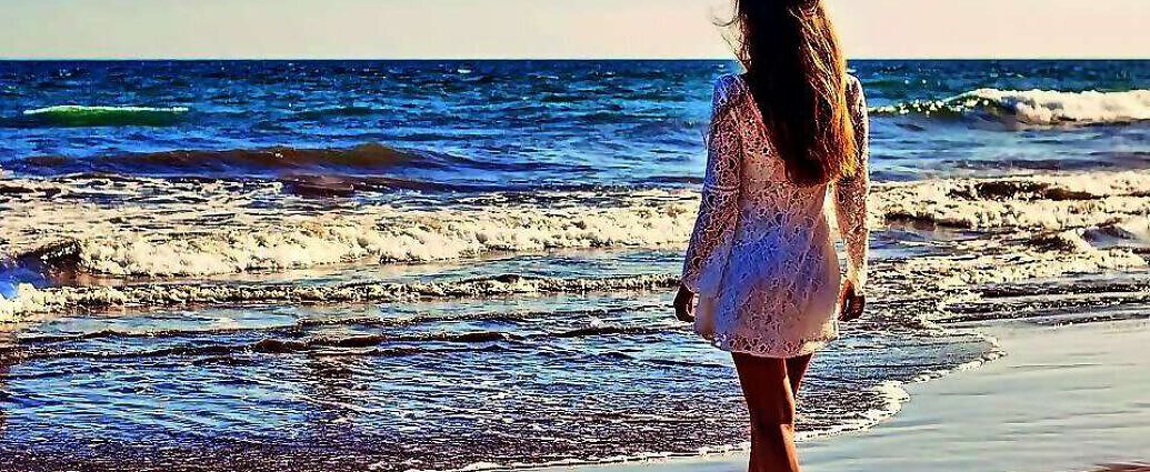 Eine Frau steht am Meer in weißen Kleid