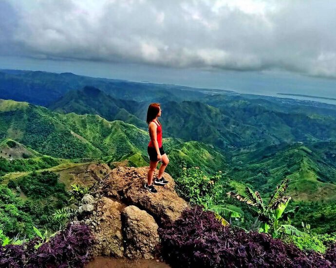 Eine junge Frau steht auf einem Berggipfel und schaut in die Ferne.