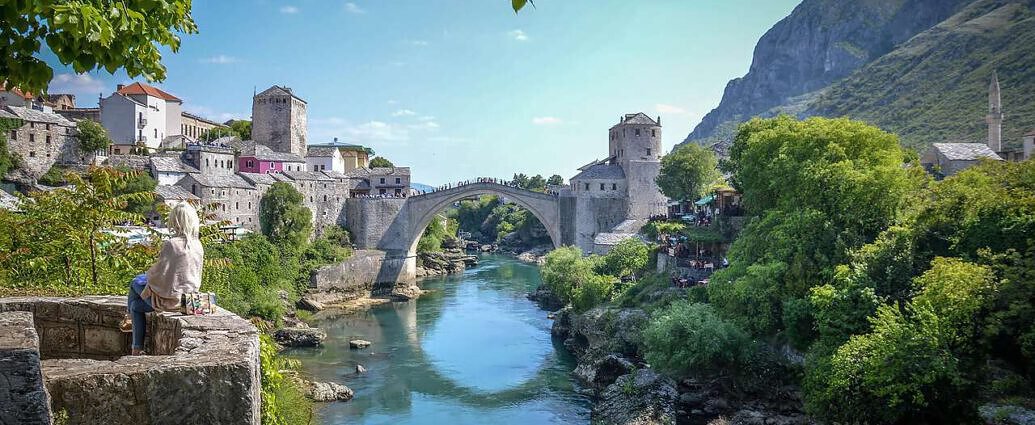 Ein Bild von Herzegowina mit Fluss und Brücke sowie der schönen Landschaft mit den alten Gebäuden.