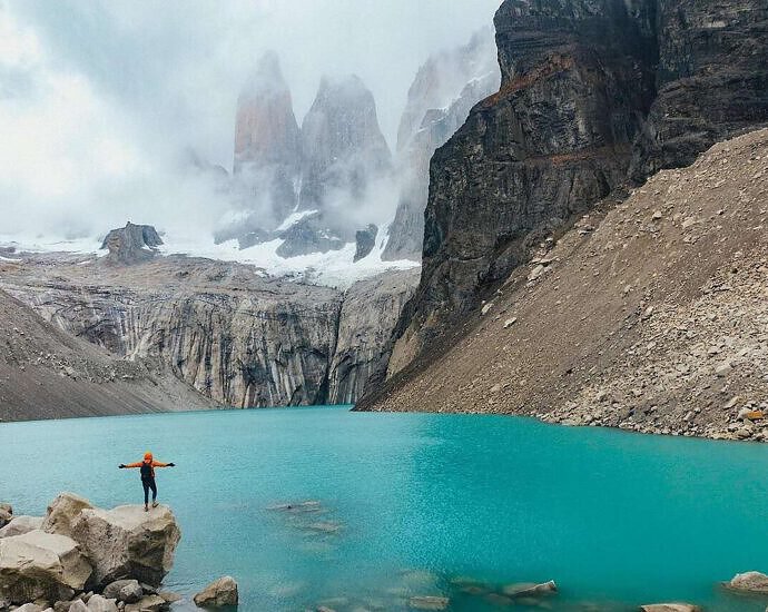 Eine junge Frau steht auf einer kleinen Klippe in Chile-Patagonien. Vor ihr erstreckt sich eine Landschaft aus Eisbergen.