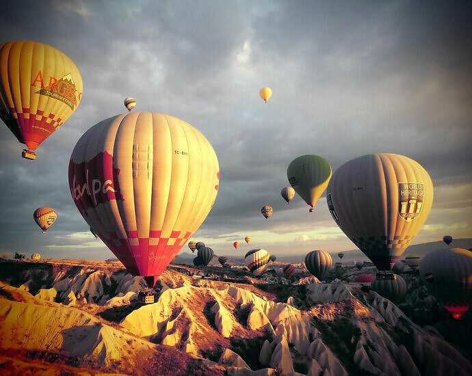 Die ersten Sonnenstrahlen brechen über die Tuffsteinfelsen Kappadokiens herein. Hundert Heißluftballons steigen lautlos und majestätisch in den Morgenhimmel und bewegen sich in perfekter Harmonie mit dem Wind. In der Türkei.