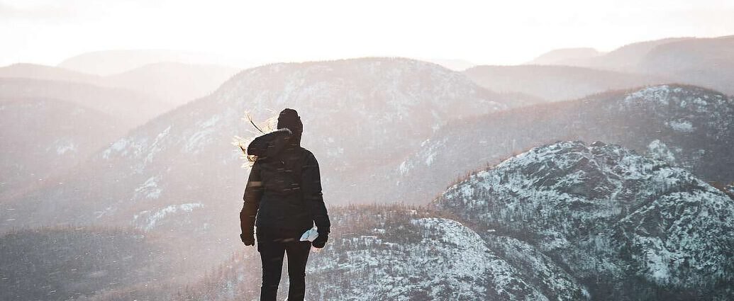 Eine junge Frau steht am Rand eines Felsvorsprunges und schaut auf die Berge.