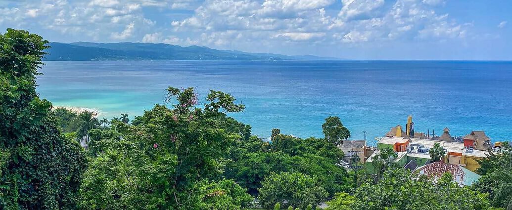 Ein Bild von Jamaika, aufgenommen von einem Berghang aus, mit Blick auf ein Dorf und das Meer.