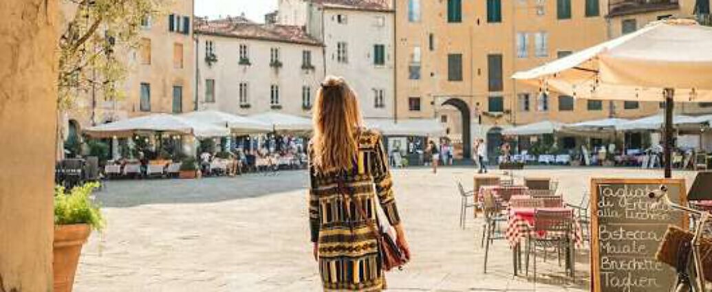 Eine junge Frau steht in einem Kleid am Torbogen von Lucca in der Toskana.