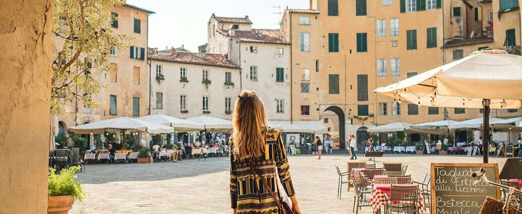 Eine junge Frau steht in einem Kleid am Torbogen von Lucca in der Toskana.