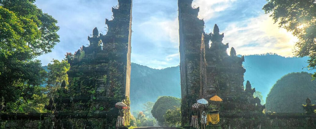Das Bild zeigt Indonesien und die Landschaft. Davor ist ein traditionelles Tor zu sehen.