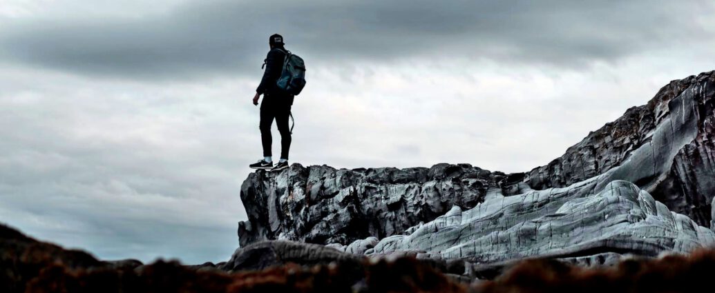 Ein Mann steht an einem Berghang und blickt in die Ferne.