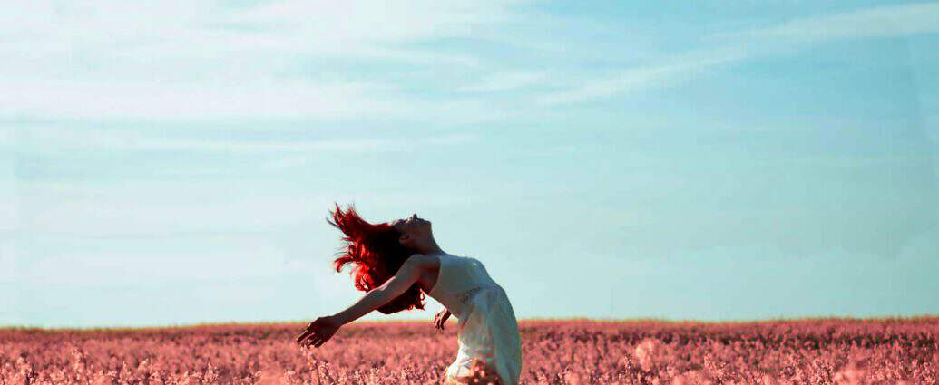 Eine junge Frau steht in einer Blumenwiese und streckt sich vor Freude.