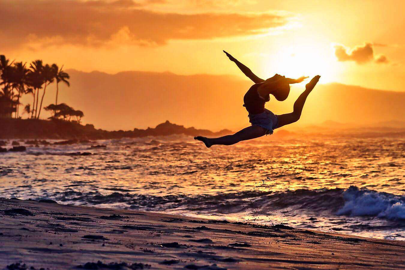 Eine junge Frau springt bei Sonnenuntergang am Meer in die Luft.