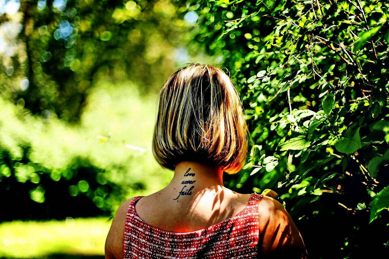 Eine Frau mit kurzen Haaren steht mit dem Rücken zu einem Wald.