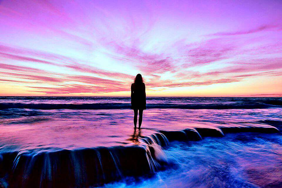 Eine Frau steht im seichten Wasser bei einem violetten Sonnenuntergang.