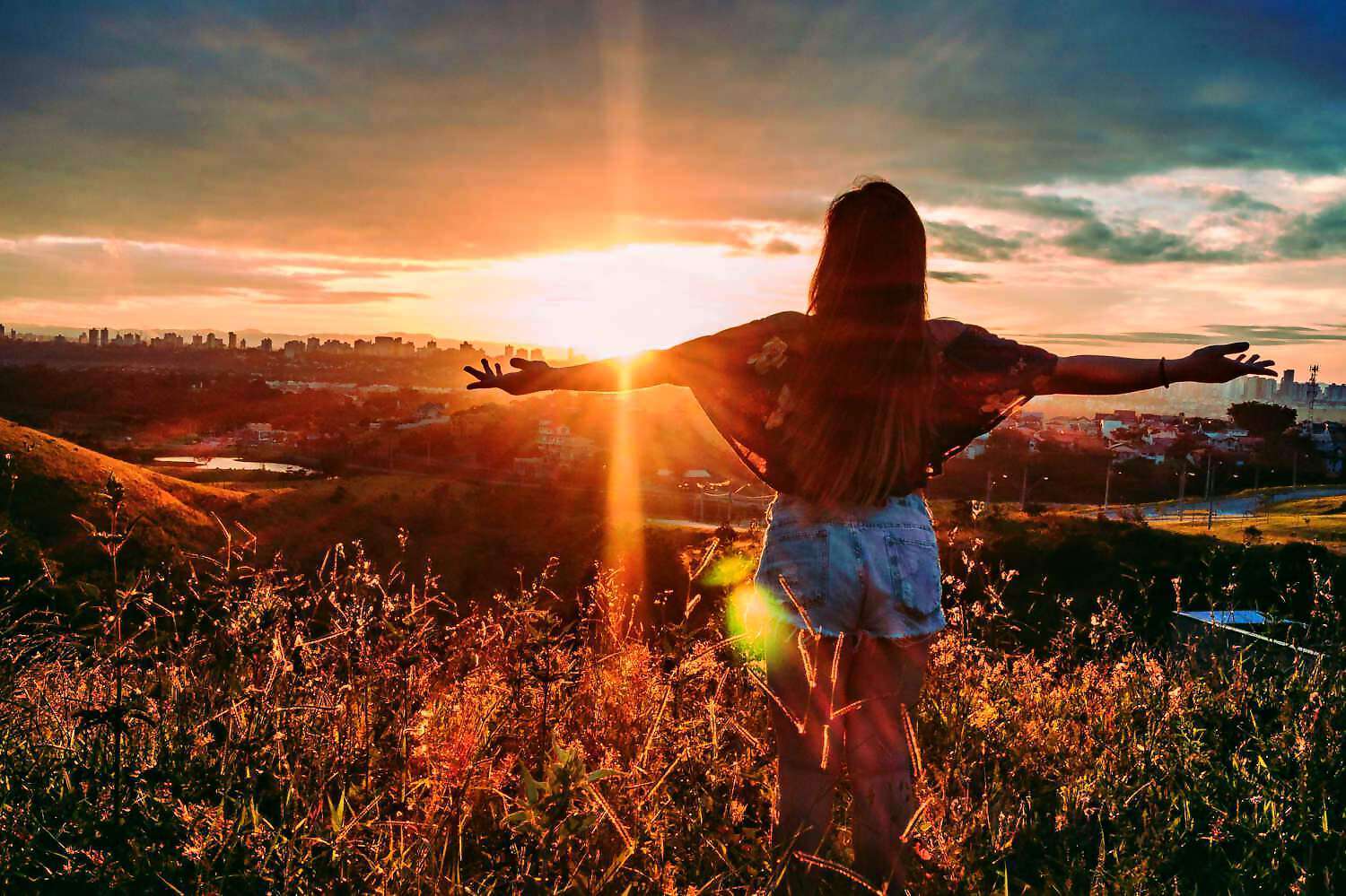 Eine junge Frau steht auf einem Feld und streckt die Arme in den Sonnenuntergang.