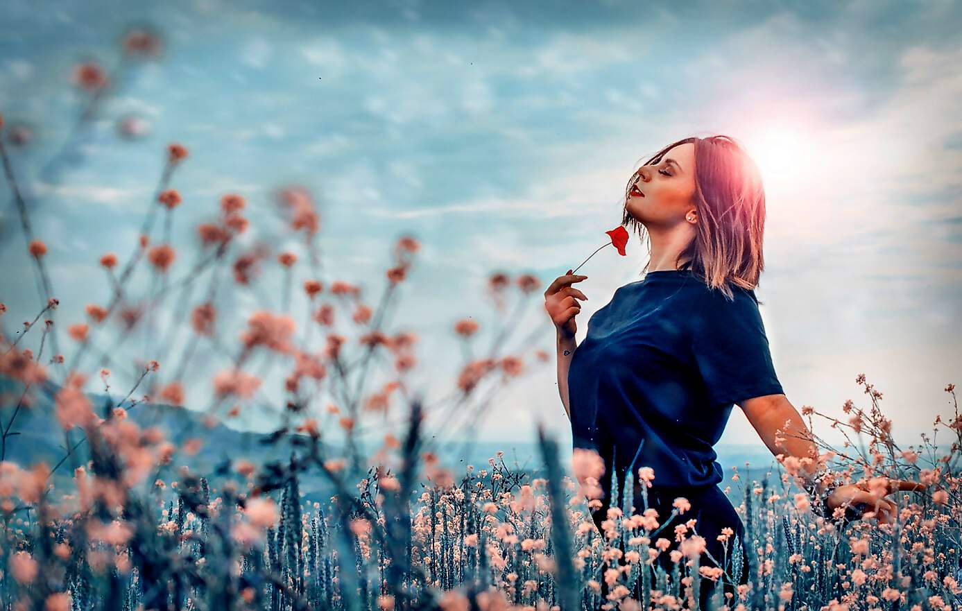 Eine schöne junge Frau steht auf einer Bergwiese und blickt vertrauensvoll in die Berge.