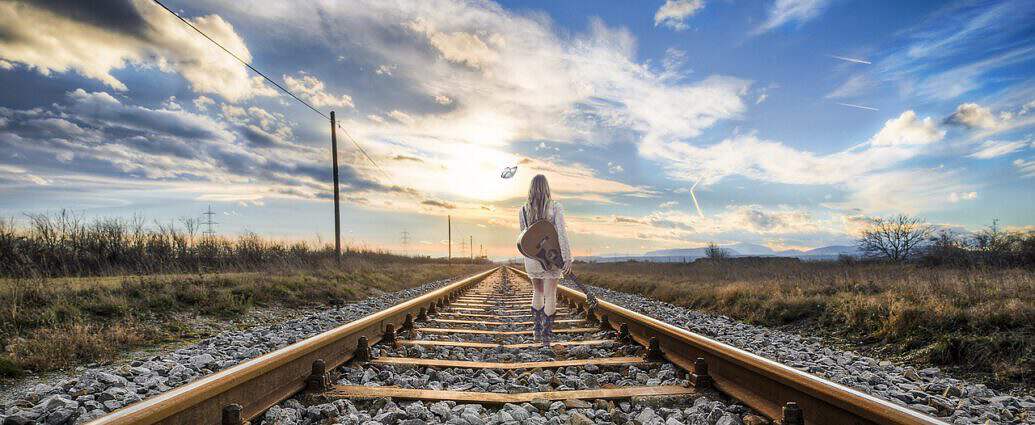 Eine junge Frau geht entlang der Gleise in Richtung Horizont.