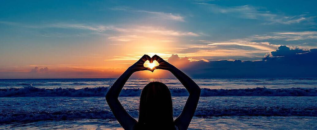 Eine Frau hält ihre Hände in Form eines Herzens in den Sonnenuntergang.