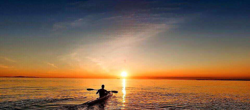 Man fährt mit Kajak dem Sonnenuntergang entgegen