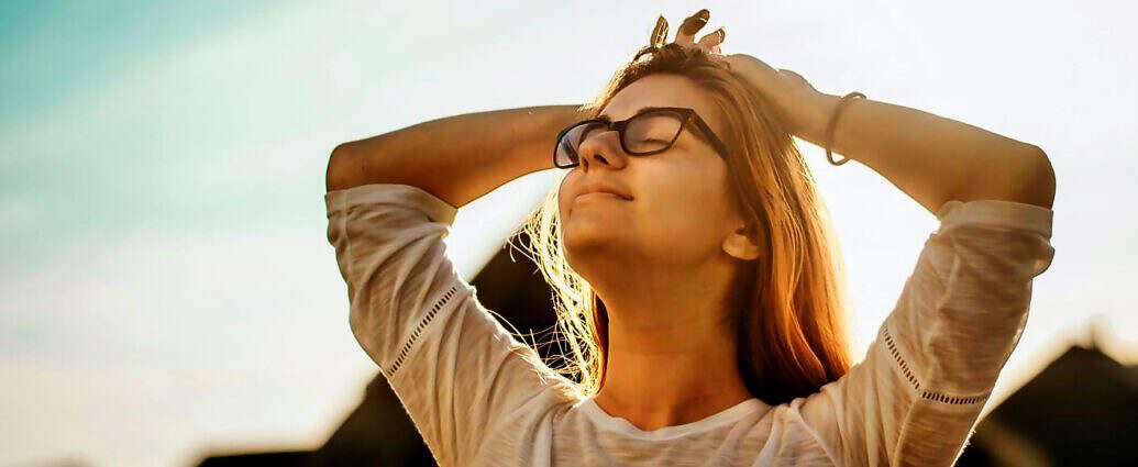 Eine junge Frau mit Brille schaut entspannt in den Himmel.