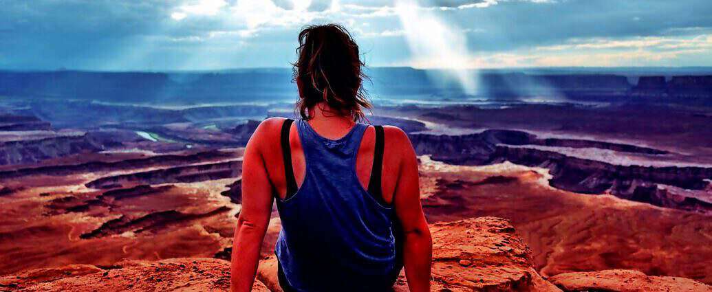 Eine junge Frau sitzt am Rande einer Schlucht und blickt geradeaus in die Ferne.