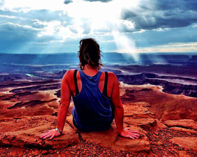 Eine junge Frau sitzt am Rande einer Schlucht und blickt geradeaus in die Ferne.