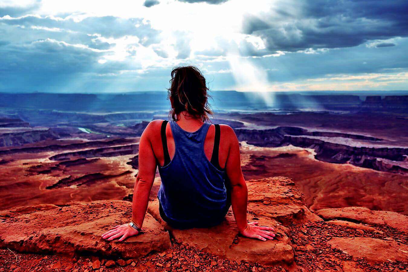 Eine junge Frau sitzt am Rande einer Schlucht und blickt geradeaus in die Ferne.