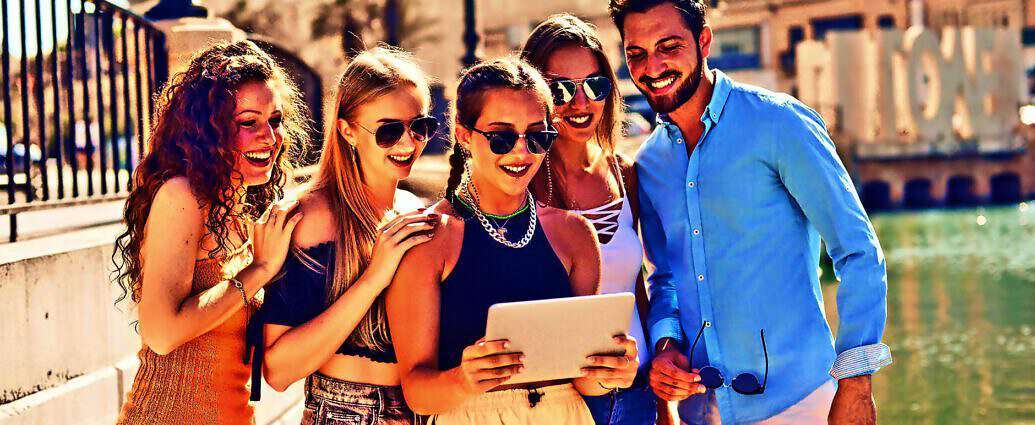 Junge Frauen und Männer stehen nebeneinander mit Blick auf ein Tablet und lachen.