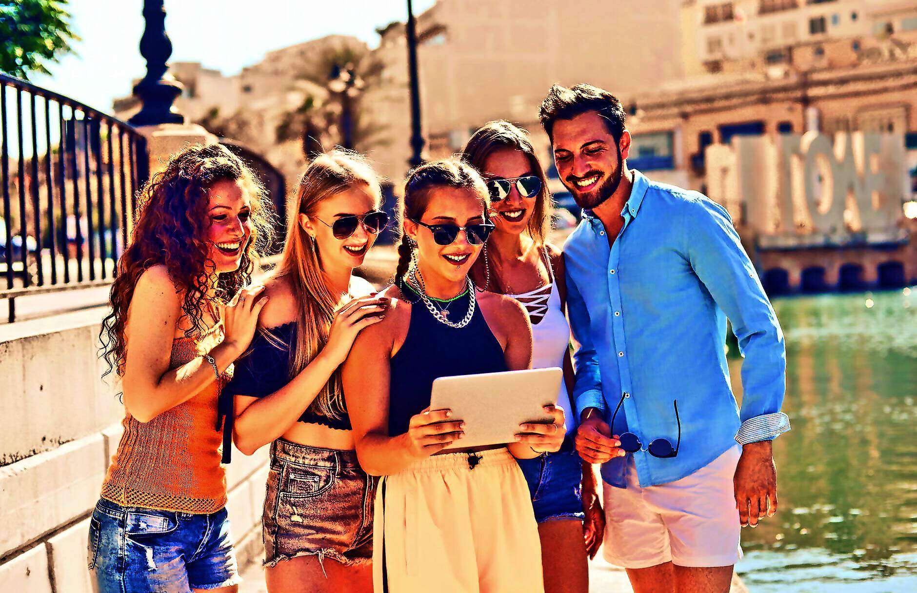 Junge Frauen und Männer stehen nebeneinander mit Blick auf ein Tablet und lachen.