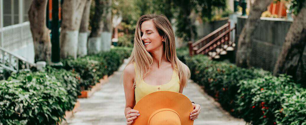 Eine junge Frau mit einem Hut in den Händen, die herzlich lacht