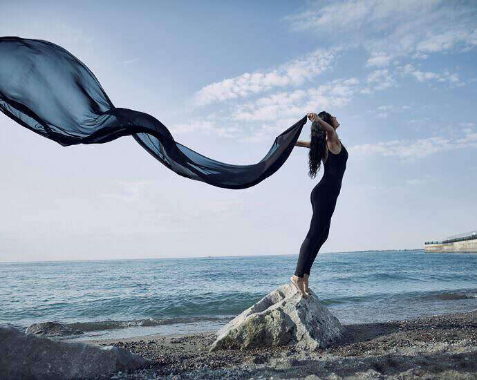 Frau steht am Meer, ein langes Seidentuch wehr im Wind