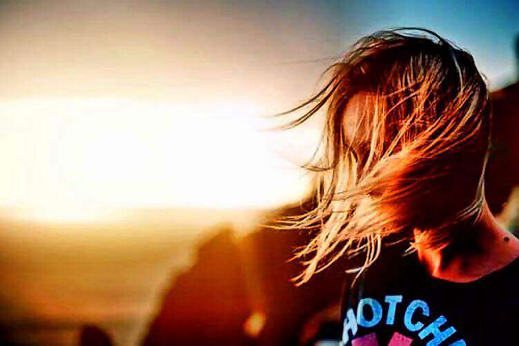 Eine junge Frau schaut verträumt in den Sonnenaufgang, ihr Haar weht leicht im Wind.