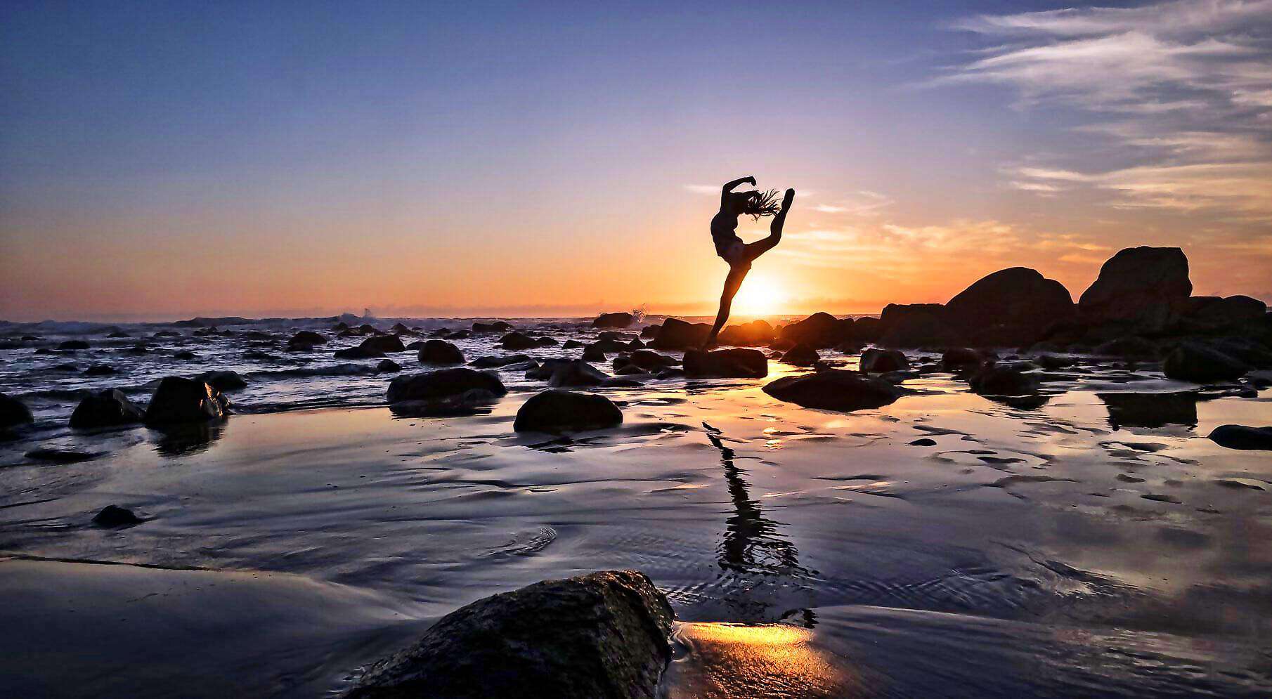 Eine junge Frau springt im flachen Wasser eines Meeres in die Luft.